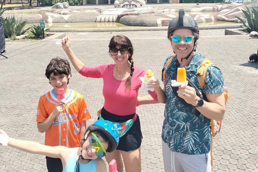 Three people outdoors, one holding a popsicle, another holding a drink, and the third holding a camera. 3