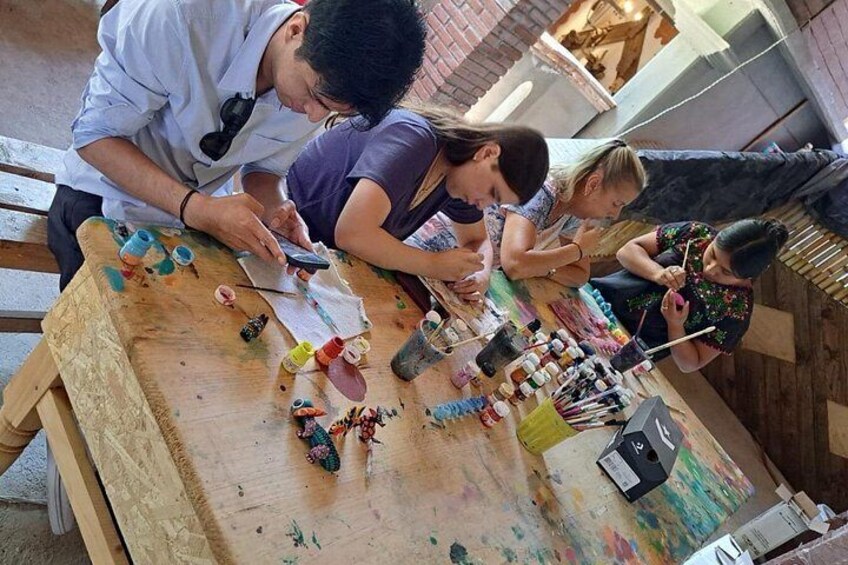 A group of people painting on a wooden table with various art supplies scattered around. 2