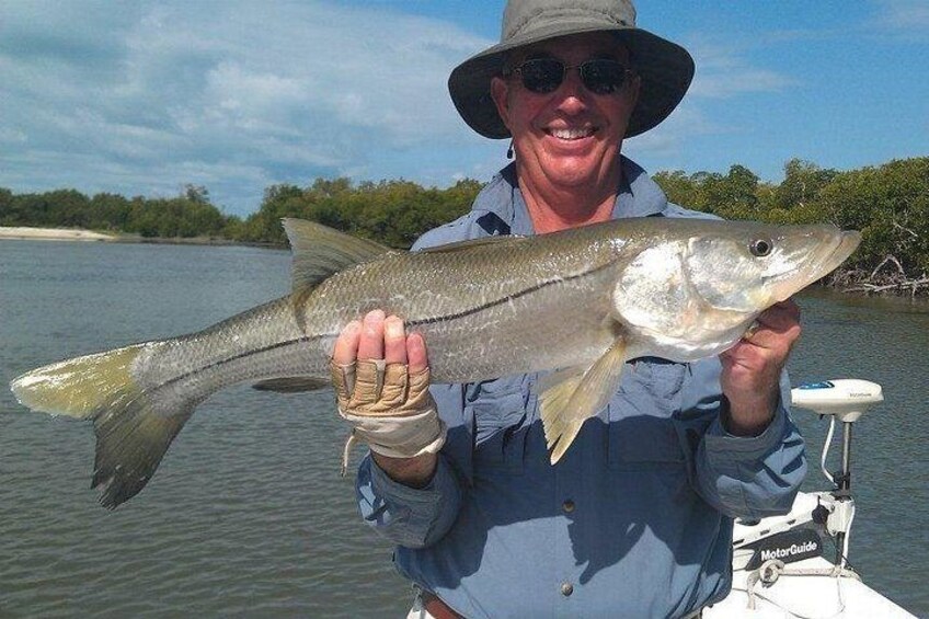 A person holding a fish by a body of water with a boat in the background. 4
