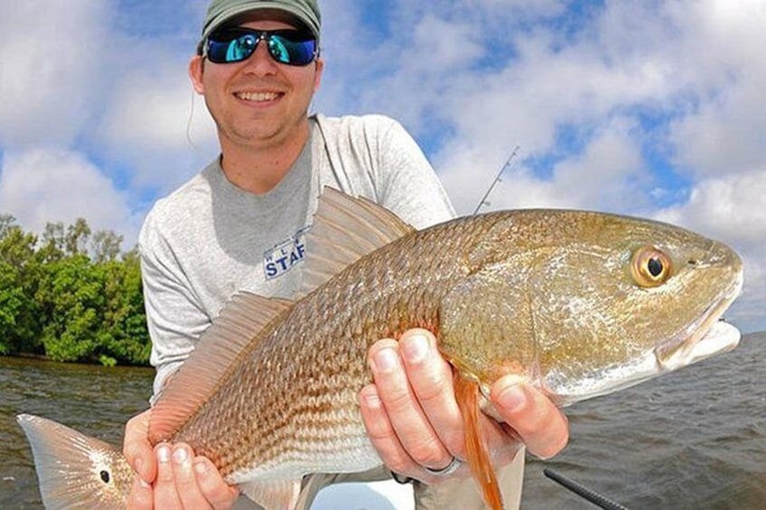 A person holding a fish with a water body and greenery in the background. 1