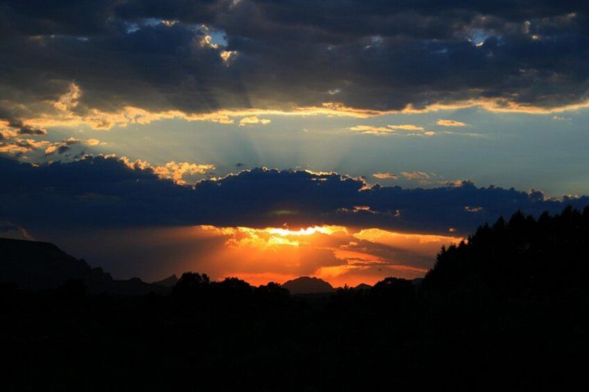 Een zonsondergang boven een bergachtig landschap met silhouetten van bomen en een heldere lucht. 3