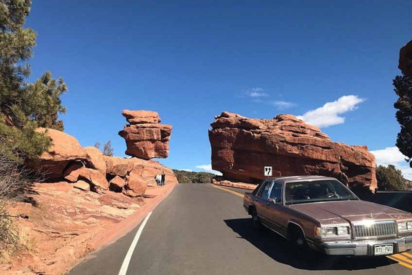 Una carretera con un automóvil, formaciones rocosas rojas y un cielo azul despejado. 3