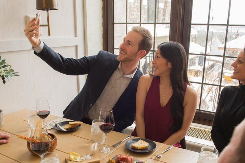 Un grupo de personas cenando en una mesa con copas de vino, platos de comida y una vela. 3