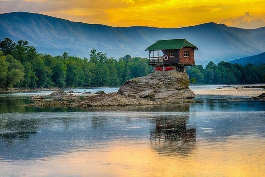 A wooden structure on a rock in a river, surrounded by trees and mountains. 2