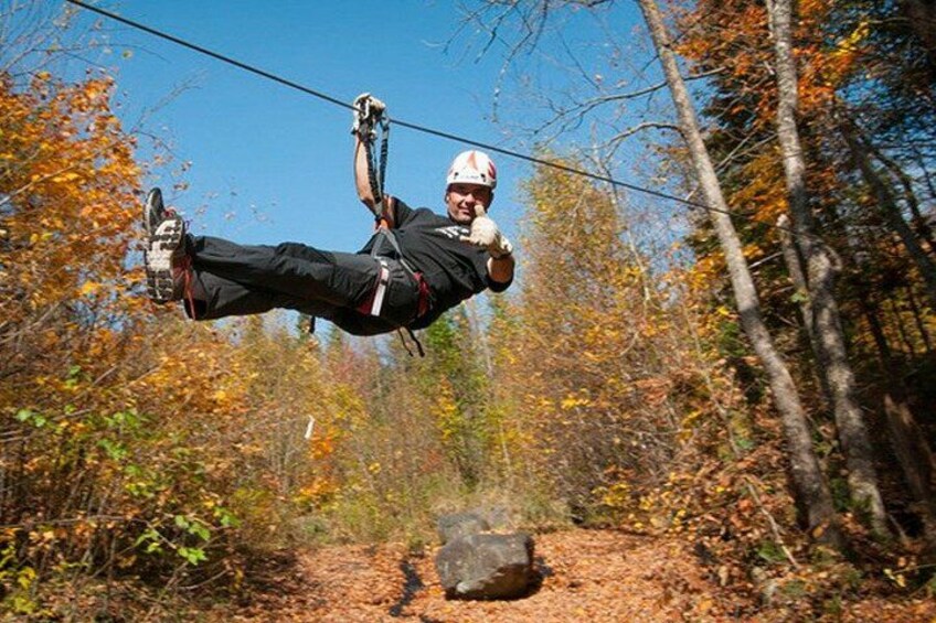 A person zip-lining through a forest with autumn foliage. 2