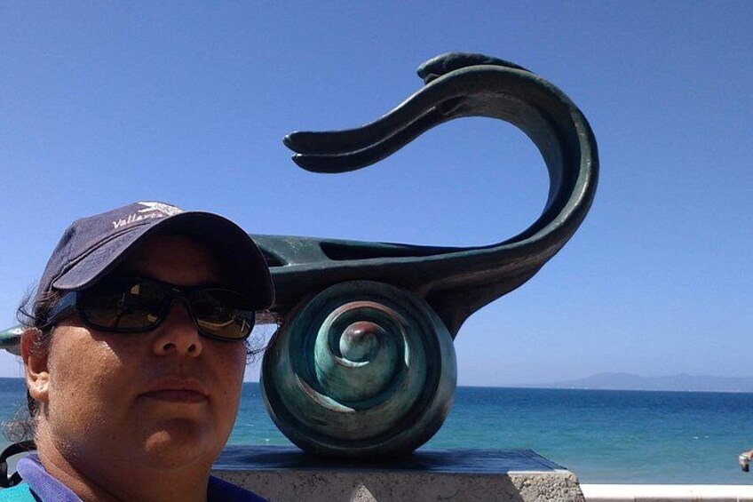 Una persona de pie frente a una escultura, con un cielo azul claro y el océano al fondo. 5