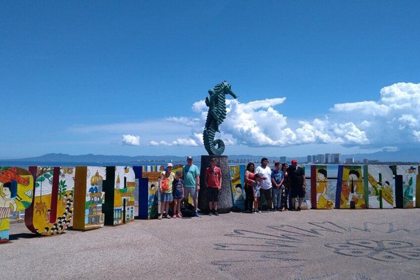 Un mural colorido con una escultura de dragón en el centro, cielo azul despejado y una ciudad lejana en la distancia. 1