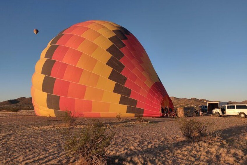 A large hot air balloon with a checkered pattern, parked on a dry, grassy field with a clear sky. 1