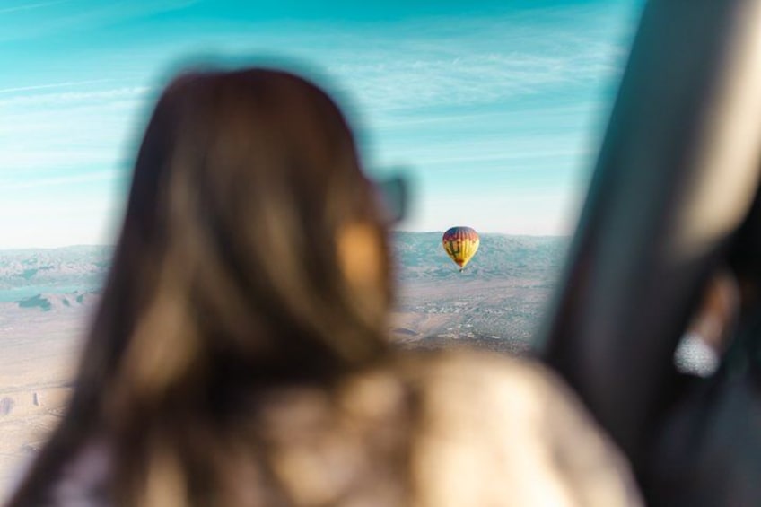 A person with long hair looking out of a window at a hot air balloon in the distance. 3