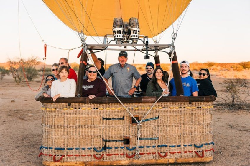 A group of people on a wicker hot air balloon in a desert landscape. 4