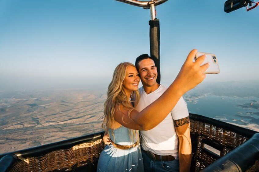 Et par tager en selfie med udsigt over en dal og bjerge i baggrunden. 1