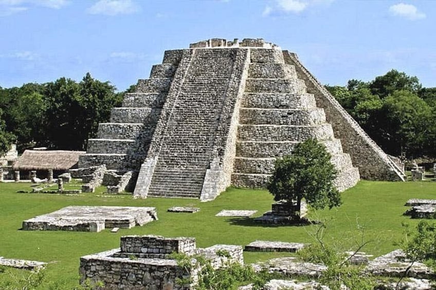 A large stone pyramid with a staircase leading to the top, surrounded by grassy areas and smaller stone structures. 1