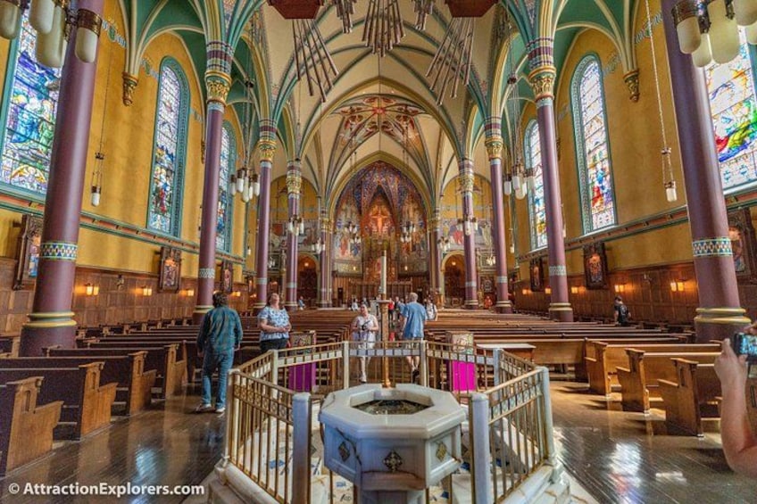 Een kerkinterieur met hoge gewelfde plafonds, glas-in-loodramen en rijen banken. 2