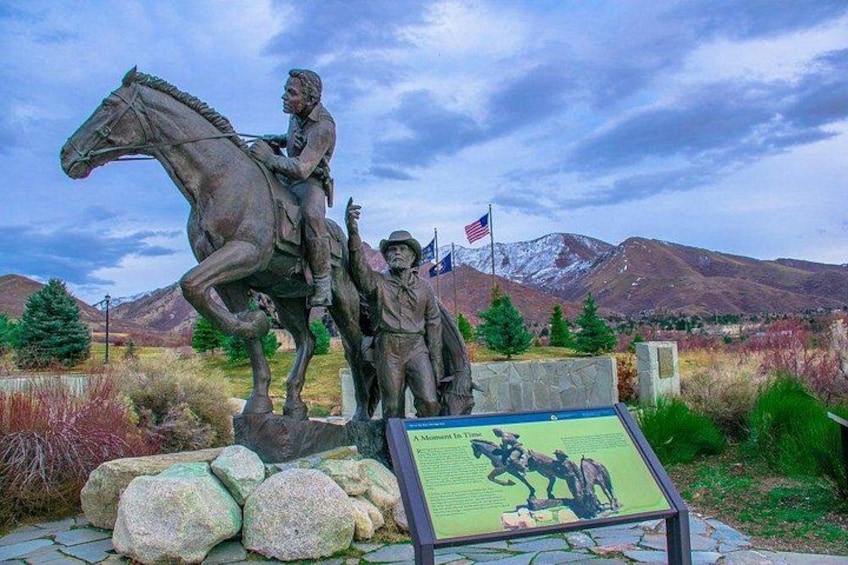 A bronze statue of a mounted figure with a child beside it, set against a mountainous backdrop. 3