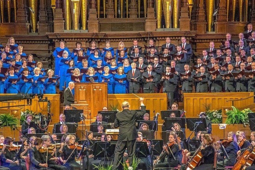 A choir and orchestra performing in a grand hall with ornate architecture. 4
