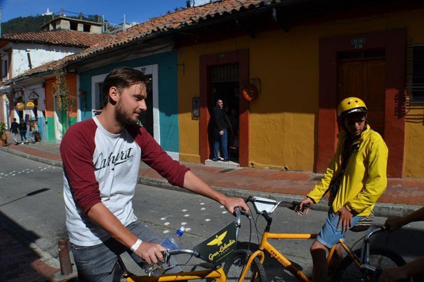 A street scene with a yellow bicycle, a person in a yellow jacket, and colorful buildings. 1