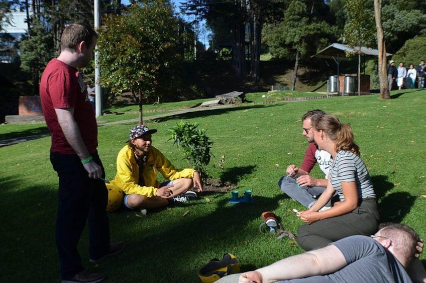A group of people sitting and standing on a grassy area with trees and a building in the background. 5