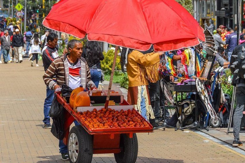 Un vendedor ambulante con un carrito lleno de tomates bajo un paraguas rojo, rodeado de peatones y otros vendedores. 3