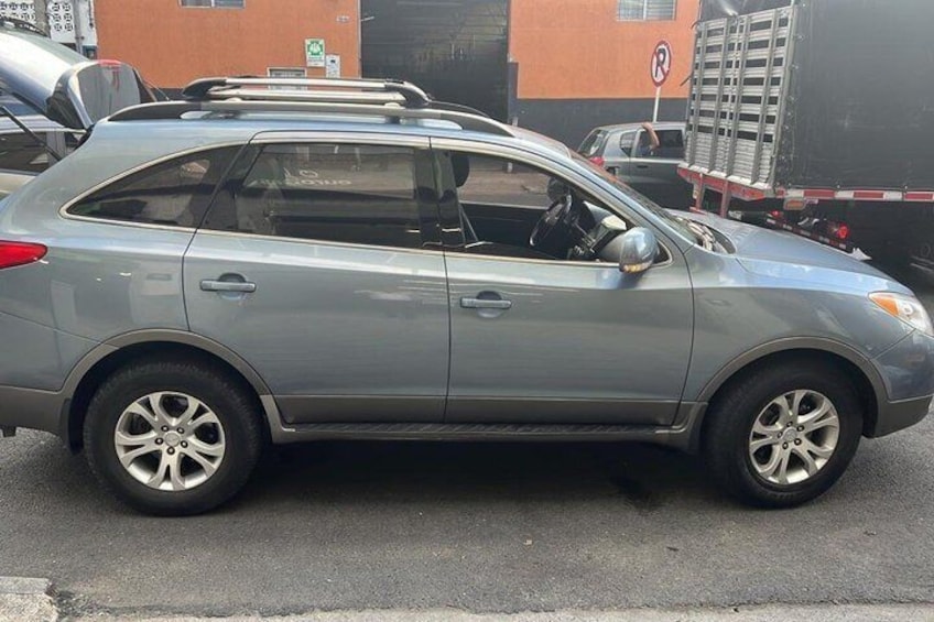 A silver SUV parked on a street with buildings and a parking sign in the background. 5