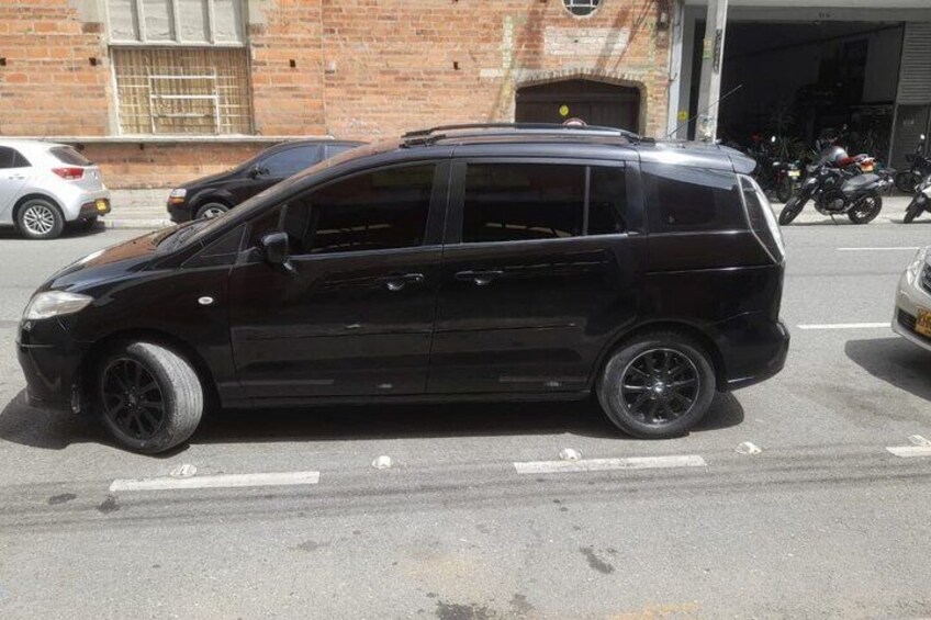A black minivan parked on a street with a brick building and parked motorcycles in the background. 3