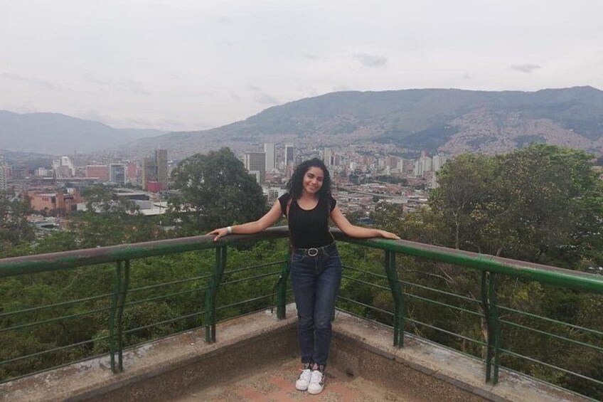 A person standing on a platform with a railing, overlooking a cityscape with mountains in the background. 4