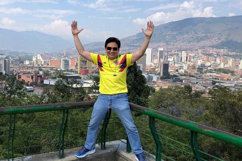 A person standing on a ledge with arms raised, overlooking a cityscape with buildings and mountains in the background. 5