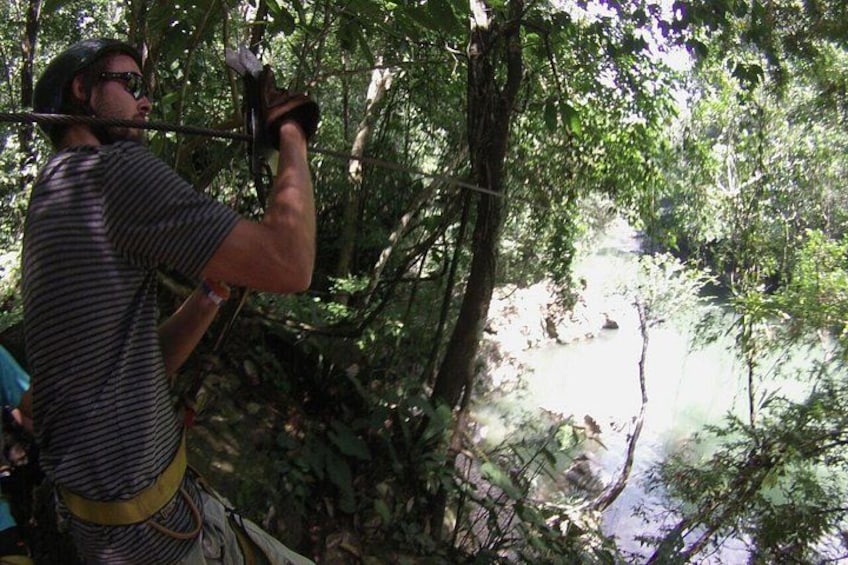 A person in a forested area, wearing a helmet and harness, preparing for a zip-lining activity. 2