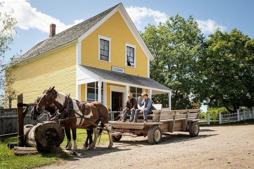 Ett gult hus med en veranda, två hästar som drar en vagn och en släpvagn med människor i. 3