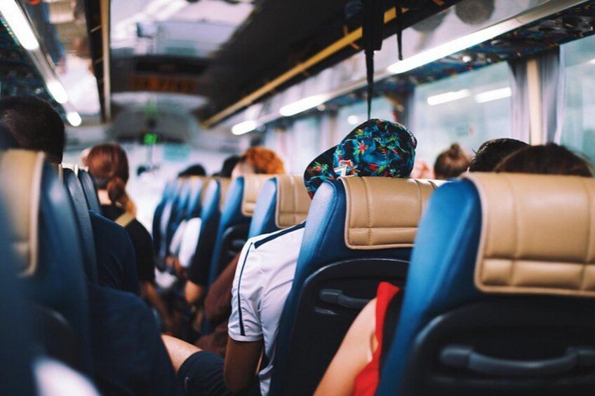 The interior of a bus with rows of seats, passengers seated, and overhead compartments. 2