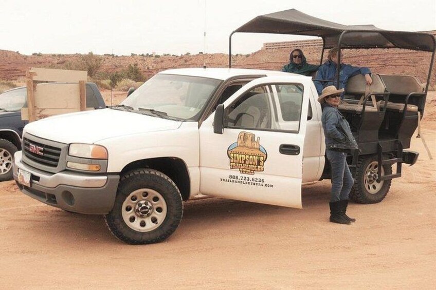 A white GMC truck with a side decal, parked in a desert with a trailer and a person standing beside it. 4