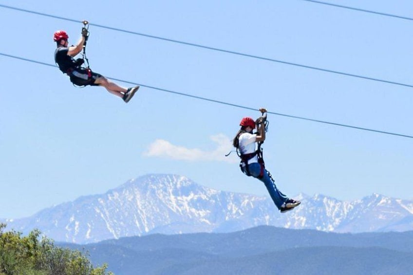 Deux personnes font de la tyrolienne au-dessus d’un paysage montagneux. 1
