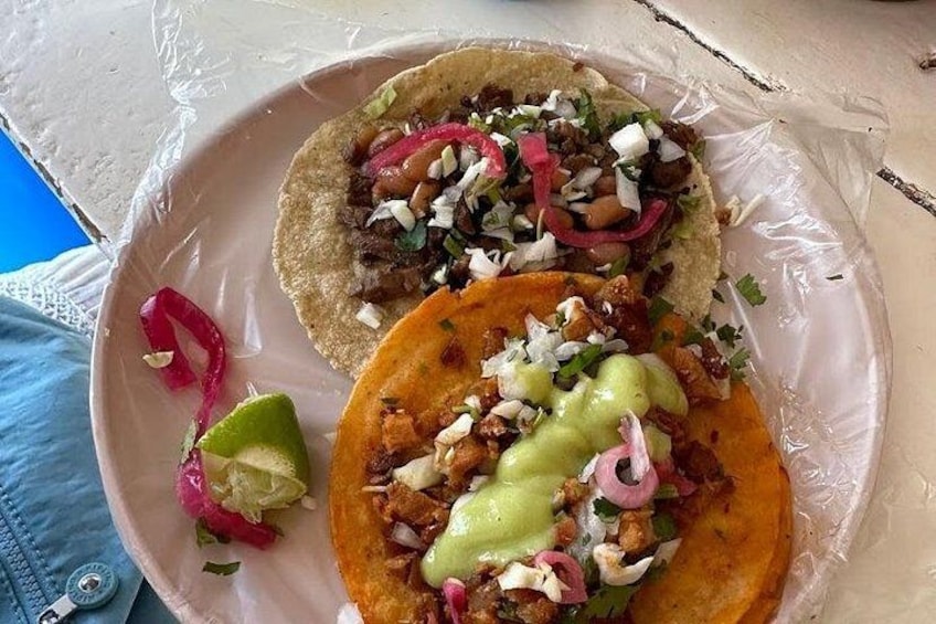 Dos tacos con ingredientes y un gajo de lima sobre un plato. 2