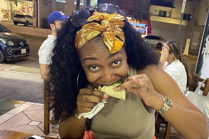 A person eating a sandwich outdoors at night. 1