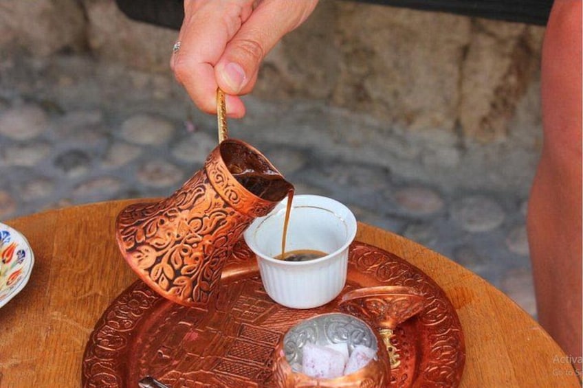 Una mano versa caffè da una caffettiera in rame in una tazza bianca su un vassoio di legno. 3