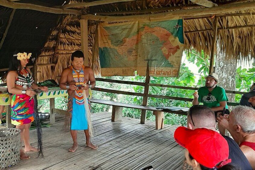 A wooden stage with a map backdrop, people in traditional attire, and a tropical setting. 3