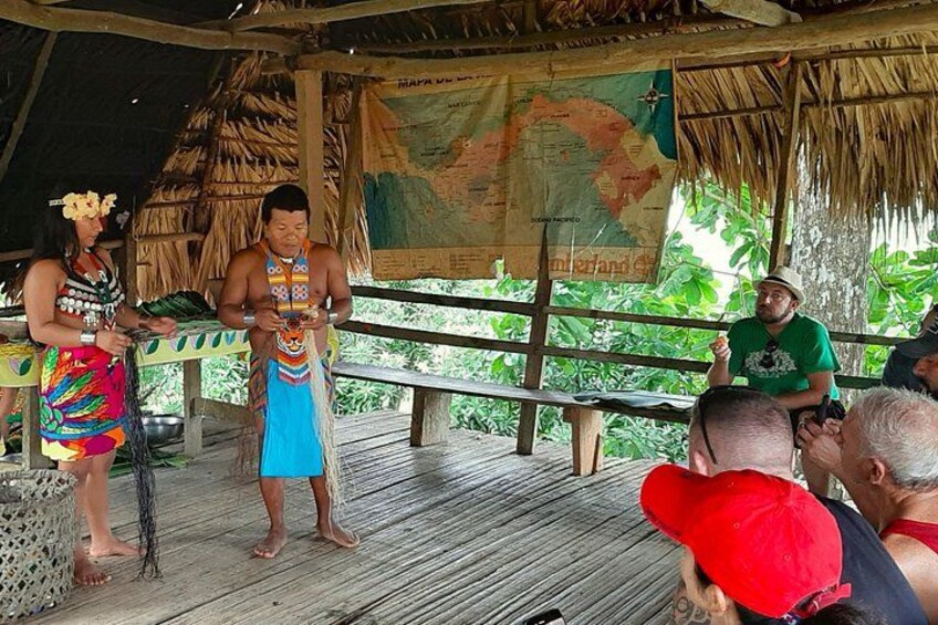 A wooden platform with a thatched roof, a map, and people in traditional attire. 4