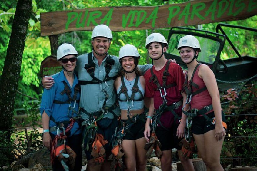 Een groep mensen met helmen en tuigjes, voor een bord met de tekst 'PURA VIDA PARADISE'. 5