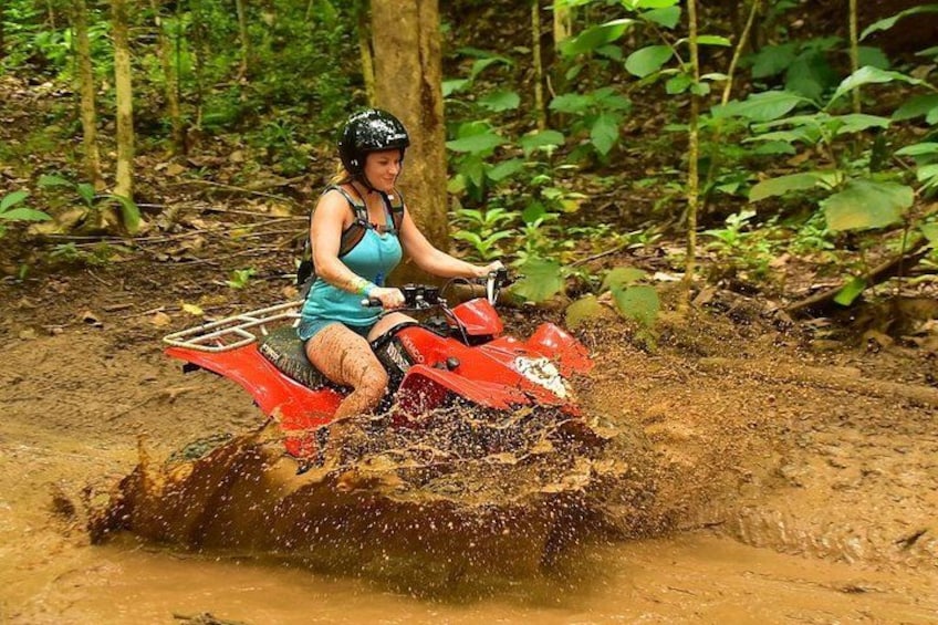 Iemand rijdt op een rode quad door een modderig terrein in een bebost gebied. 2