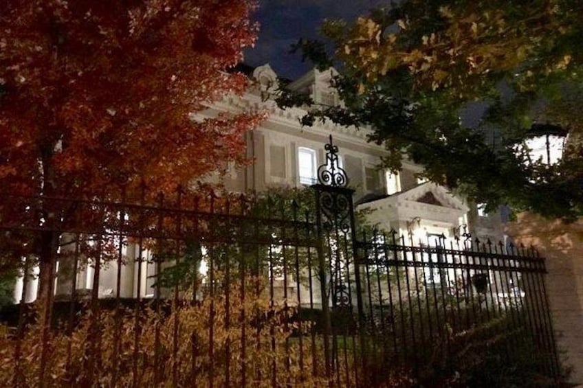 A gated building at night with autumn foliage and a lit fence. 2