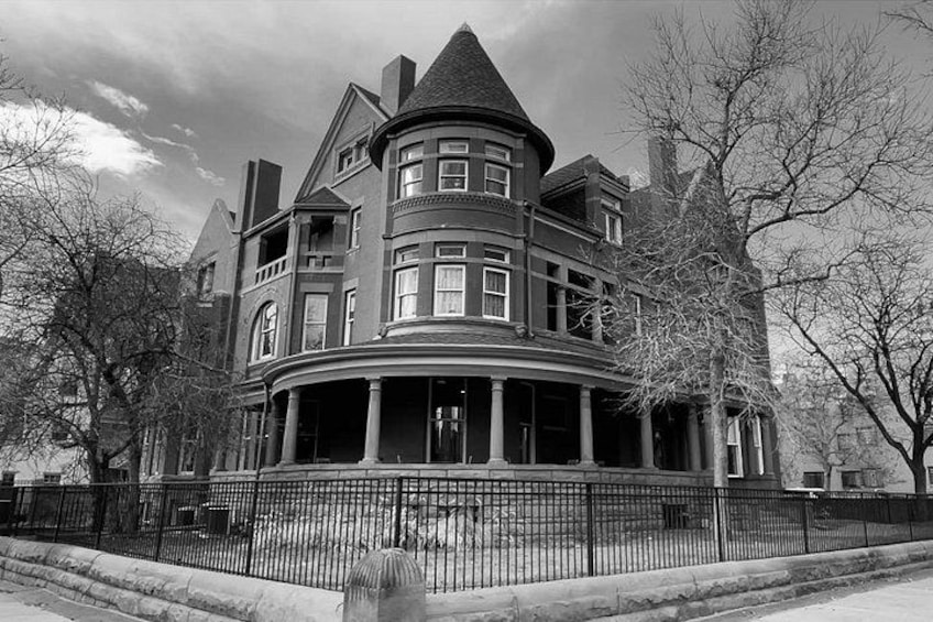 A large, historic house with a prominent turret and multiple windows, surrounded by a metal fence and leafless trees. 3