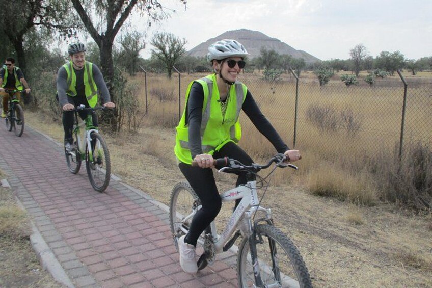 Three cyclists on a paved path with a fence and dry grass in the background. 4