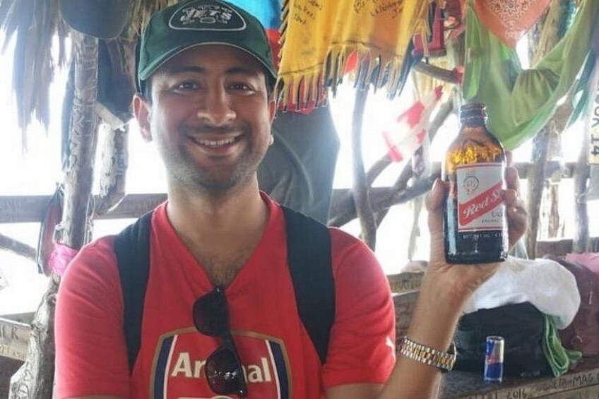 Una persona sostiene una botella de cerveza Red Stripe, lleva una camiseta roja con la inscripción 'Arsenal' y una gorra verde. 5