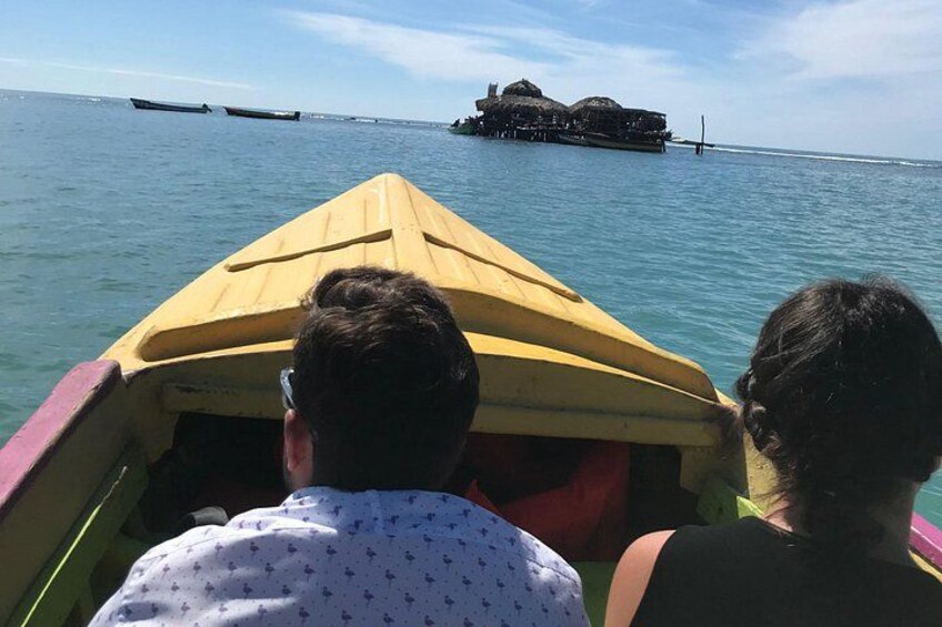 Un bote amarillo con dos personas a bordo, dirigiéndose hacia una isla distante con construcciones. 3