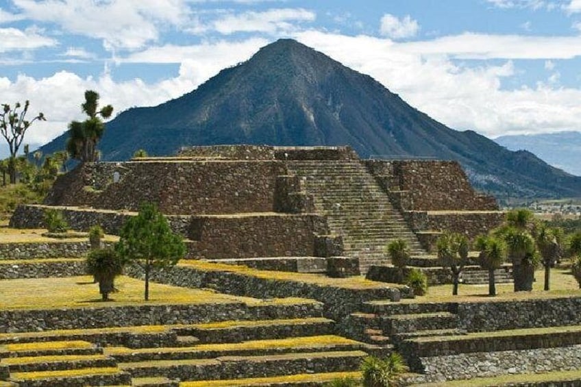 Ancient ruins with stepped pyramids, a mountain in the background, and sparse vegetation. 1