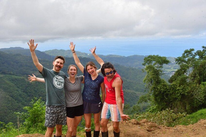 Four people standing on a hill with their arms raised, overlooking a mountainous landscape. 3