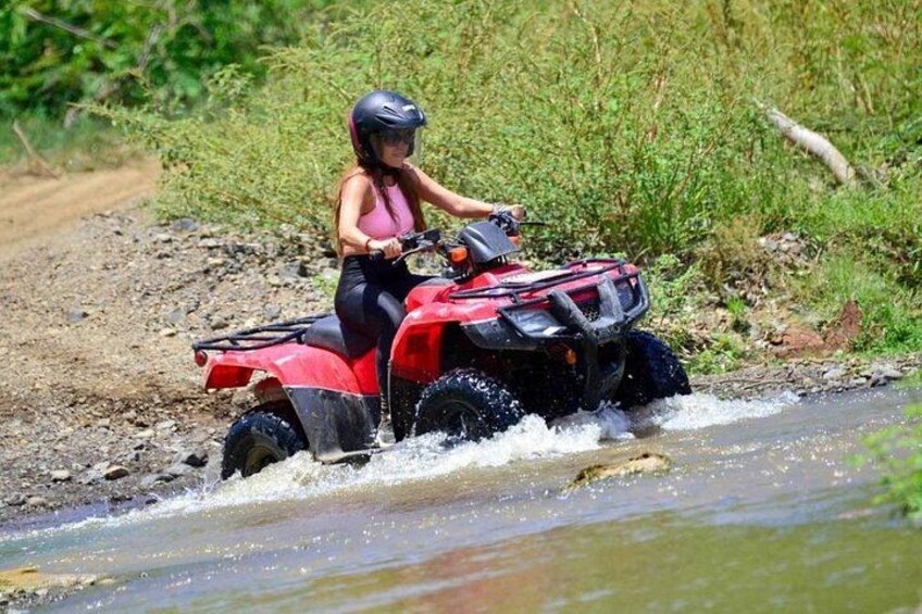 A person riding a red ATV through a shallow water crossing. 2