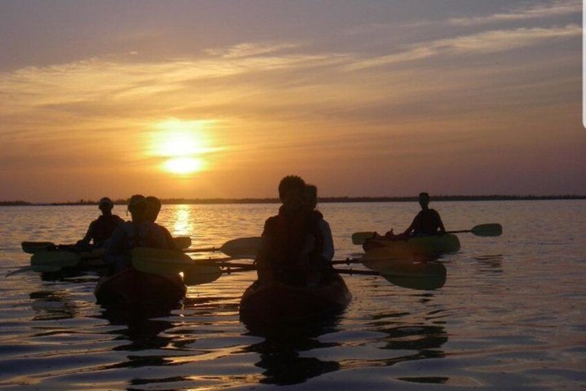 Personas haciendo kayak en un cuerpo de agua tranquilo durante la puesta de sol. 2