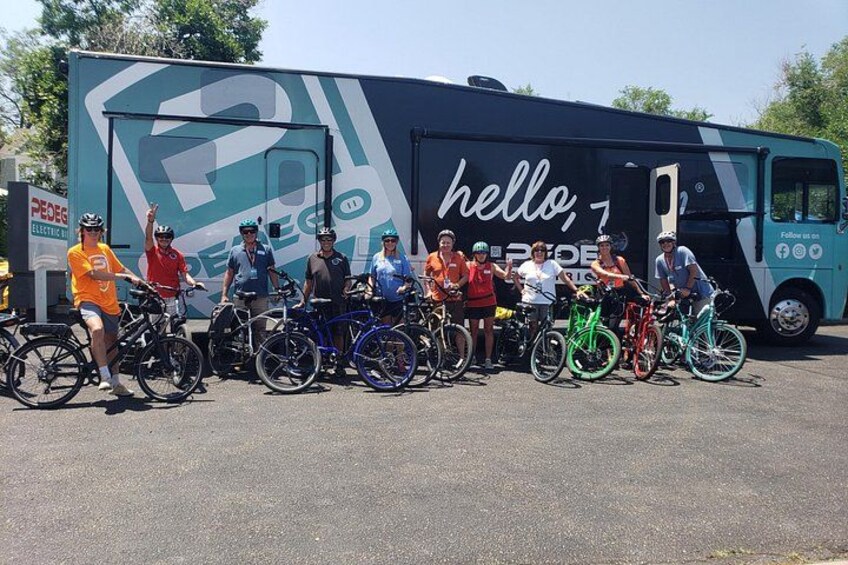 Un grupo de ciclistas posando frente a un autobús grande con un cartel que dice 'hello'. 2