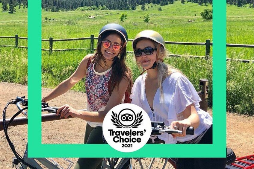 Two people on bicycles in a rural setting with green fields and a wooden fence. 1