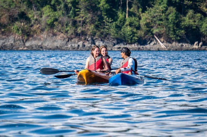 Trois personnes pratiquent le kayak sur une étendue d’eau calme, avec une rive boisée en arrière-plan. 5